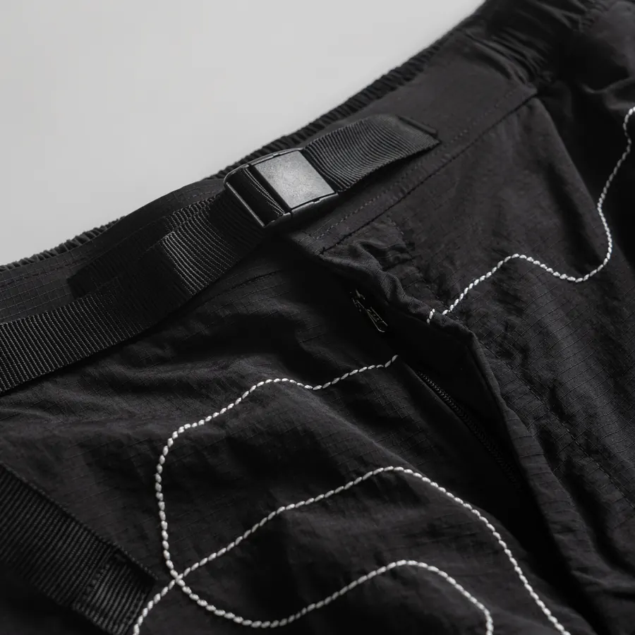 Sabuk webbing dan buckle di pinggang celana pendek, dengan garis jahitan putih.
