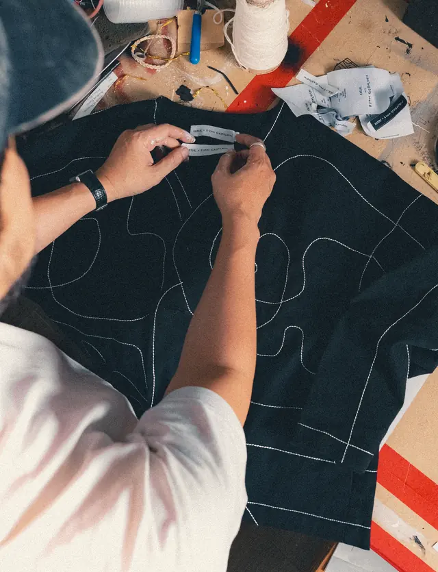 Label co-brand diletakkan di jaket hitam dengan garis jahitan putih.
